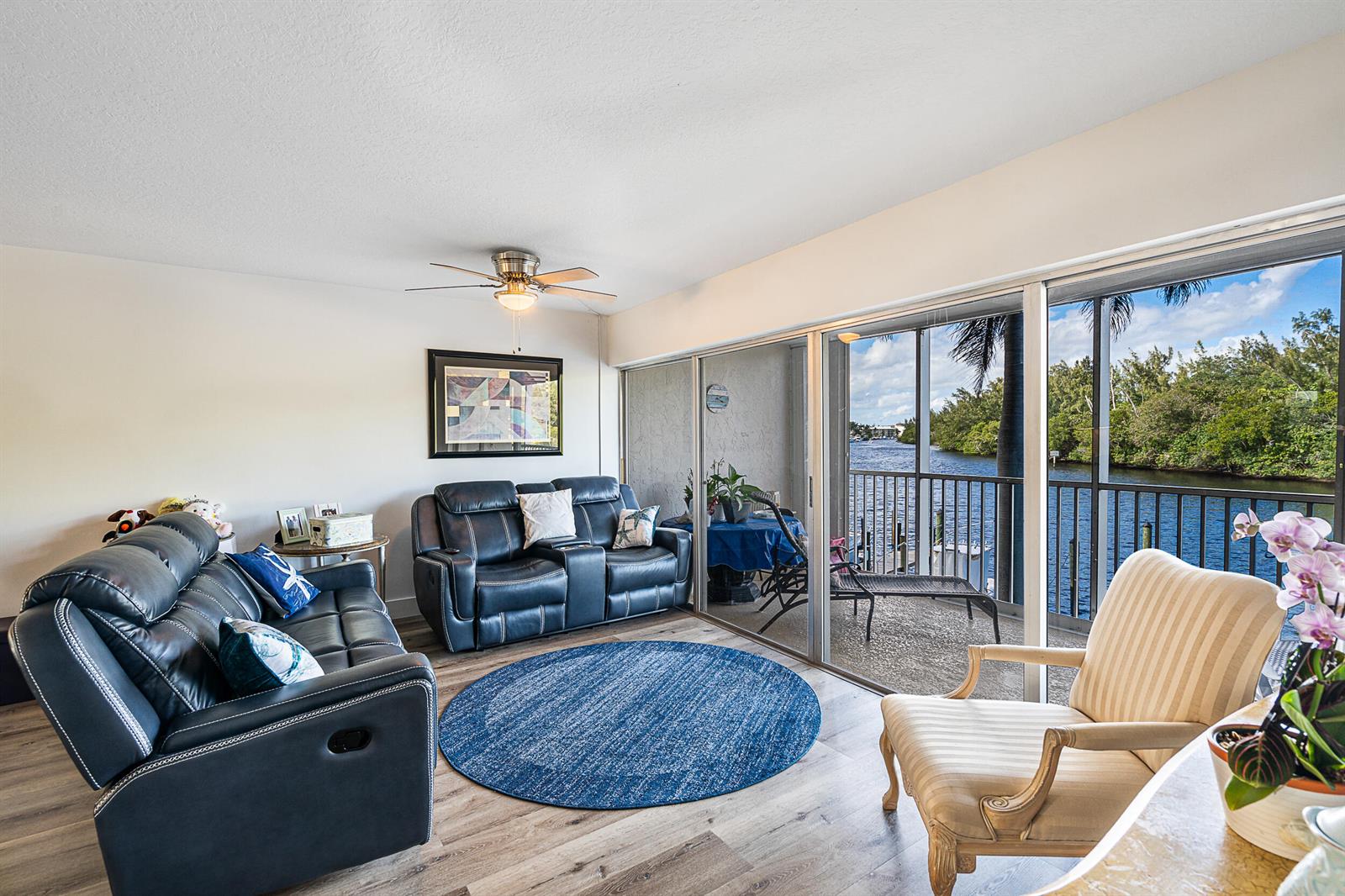 A living room features dark leather sofas, a blue rug, and a balcony overlooking water — 1537 E Hillsboro Boulevard # 243, Deerfield Beach FL 33441, DEERFIELD BEACH, FL