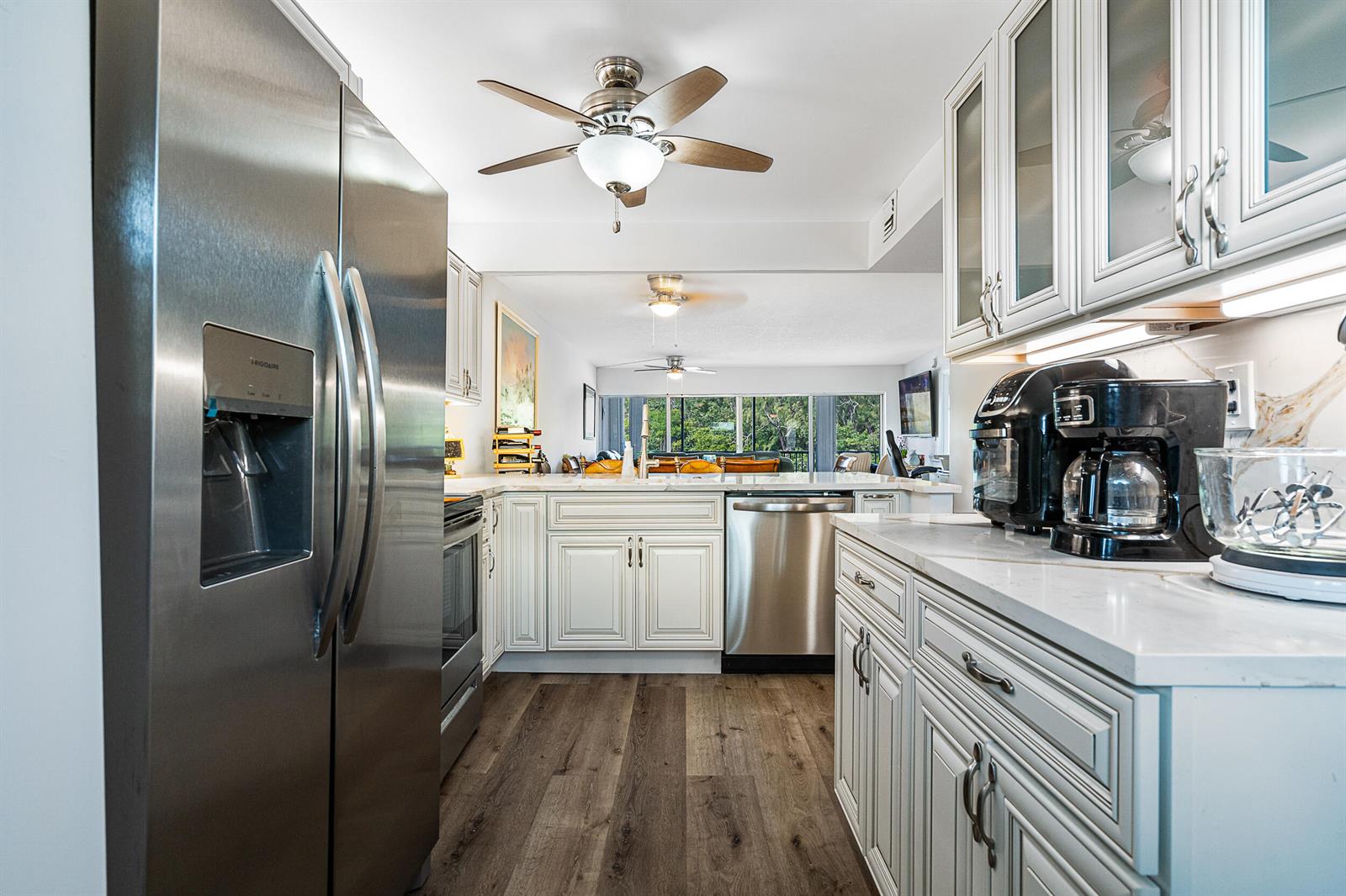 A kitchen with stainless steel appliances, white cabinetry, and wood-look flooring opens to a living area — 1537 E Hillsboro Boulevard # 243, Deerfield Beach FL 33441, DEERFIELD BEACH, FL