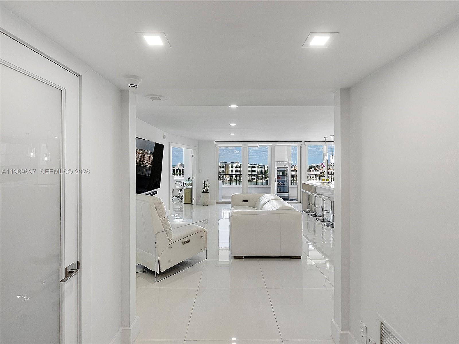A white-tiled living room features a modern sofa, a recliner, and a kitchen island — 550 S Ocean Blvd # 1509, Boca Raton FL 33432, BOCA RATON, FL