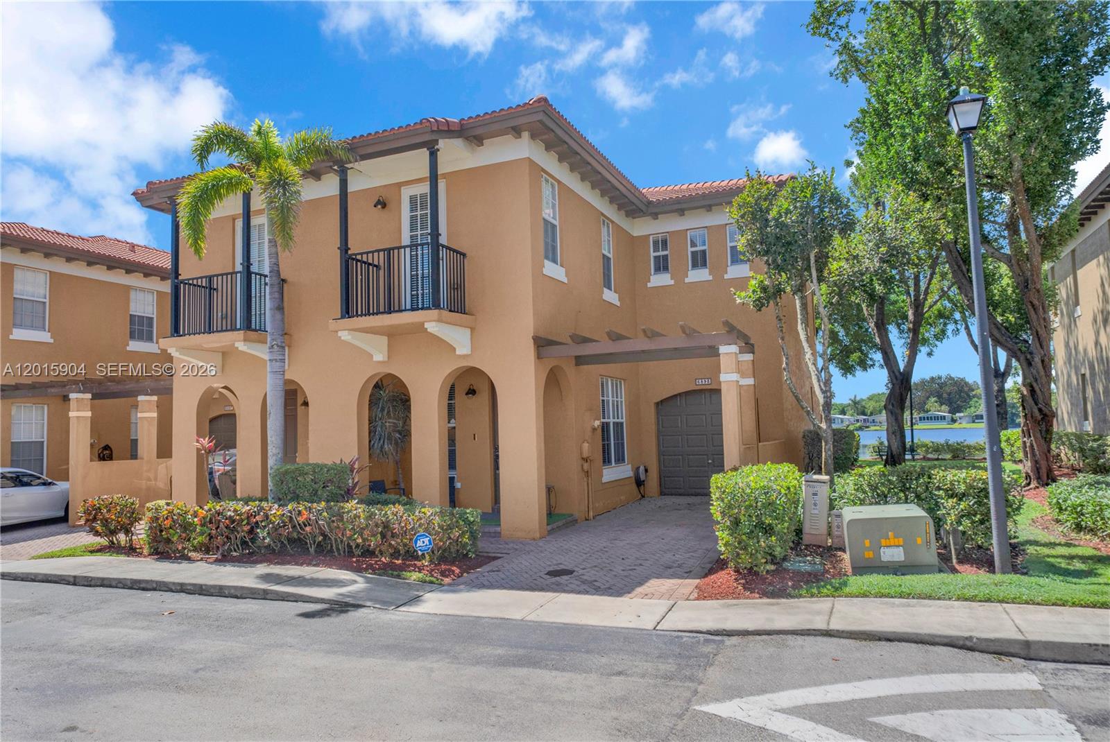 A two-story stucco house with a tile roof, balcony, and attached garage sits on a street — 6893 Julia Gardens Dr, Coconut Creek FL 33073, COCONUT CREEK, FL