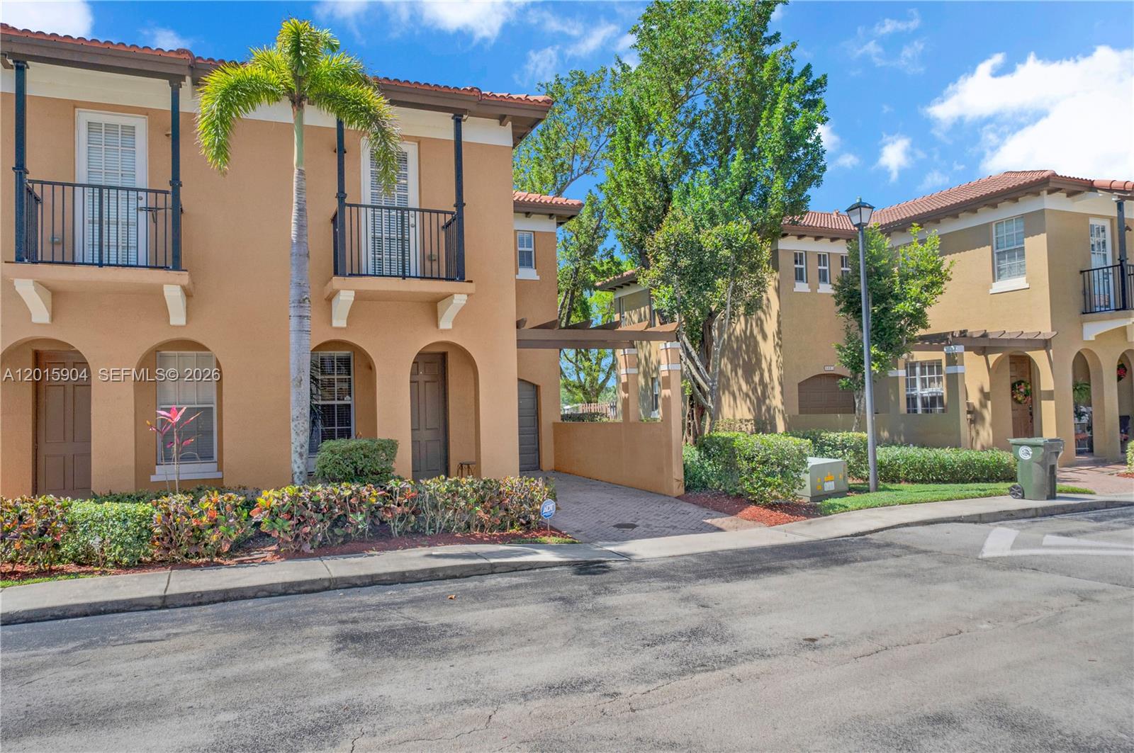 Exterior view of two-story tan stucco townhouses with balconies and a paved driveway — 6893 Julia Gardens Dr, Coconut Creek FL 33073, COCONUT CREEK, FL