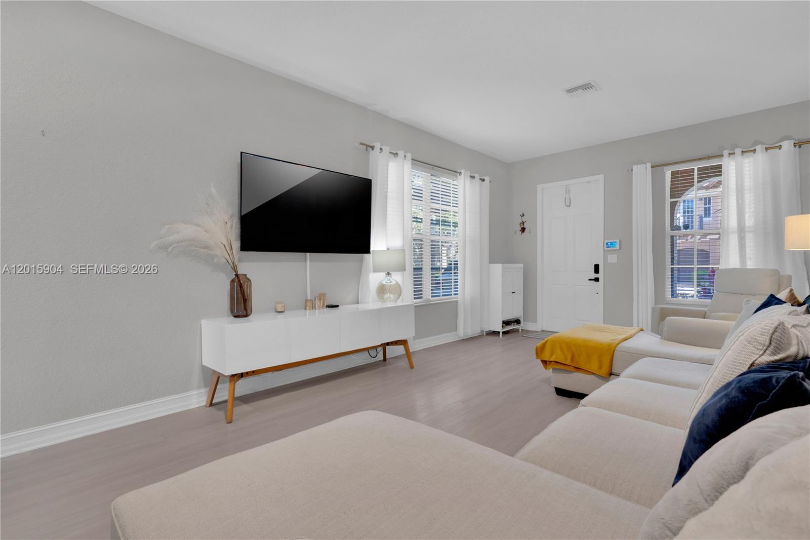 A living room features light gray walls, wood-look flooring, a white media console, and a sectional — 6893 Julia Gardens Dr, Coconut Creek FL 33073, COCONUT CREEK, FL
