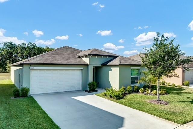 A single-story house with a light green exterior, a two-car garage, and a concrete driveway — 6727 BAR S BAR TRAIL, ZEPHYRHILLS, FL