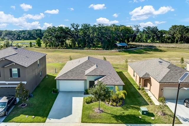 An aerial view shows three suburban houses with driveways and lawns near a grassy field — 6727 BAR S BAR TRAIL, ZEPHYRHILLS, FL