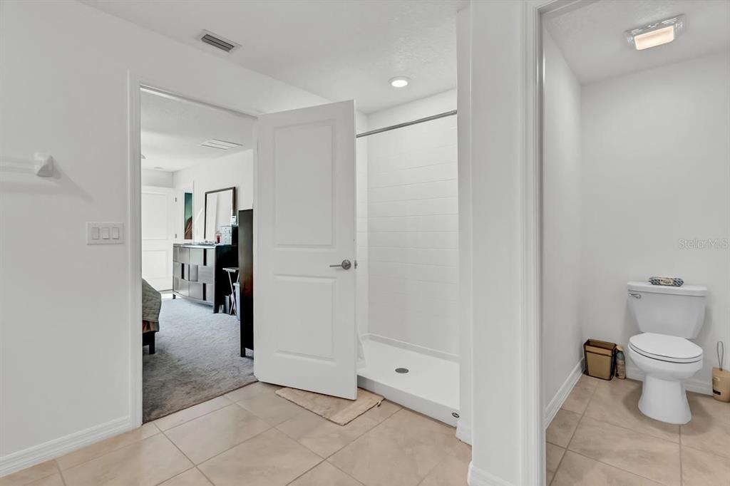 A bathroom with a walk-in shower, tile flooring, and a toilet, opening into a bedroom — 6727 BAR S BAR TRAIL, ZEPHYRHILLS, FL