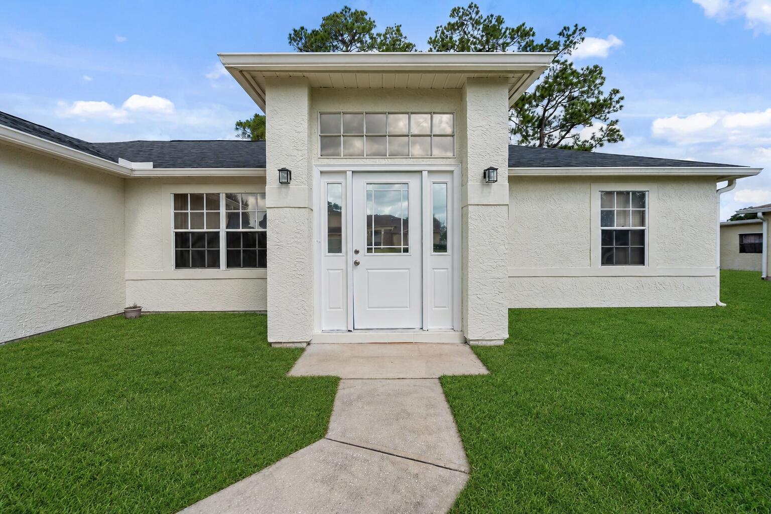 The exterior of a single-story house features a white stucco facade, a central entryway, and a walkway — 349 Hammock Road SE, Palm Bay FL 32909, PALM BAY, FL