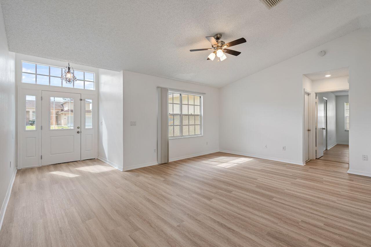 An empty living room features light wood-look flooring, white walls, and a ceiling fan — 349 Hammock Road SE, Palm Bay FL 32909, PALM BAY, FL