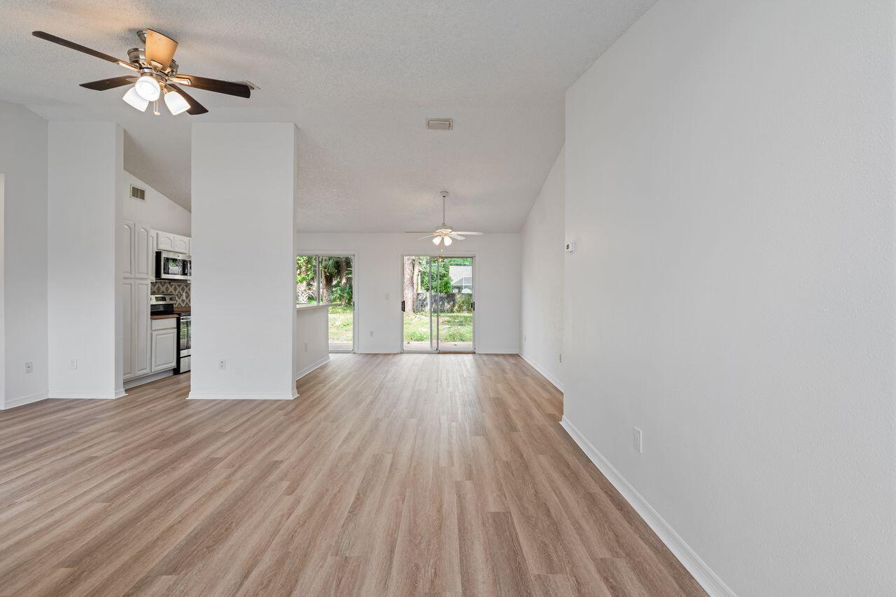 An open-concept living and dining area features light wood-look flooring, white walls, and ceiling fans — 349 Hammock Road SE, Palm Bay FL 32909, PALM BAY, FL
