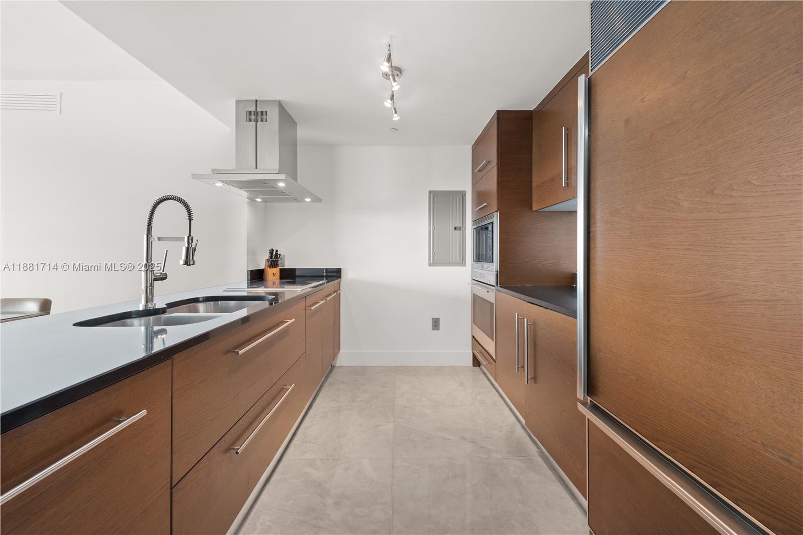 A modern galley kitchen features wood cabinetry, stainless steel appliances, and dark countertops — 495 Brickell Ave # 5003, Miami FL 33131, MIAMI, FL