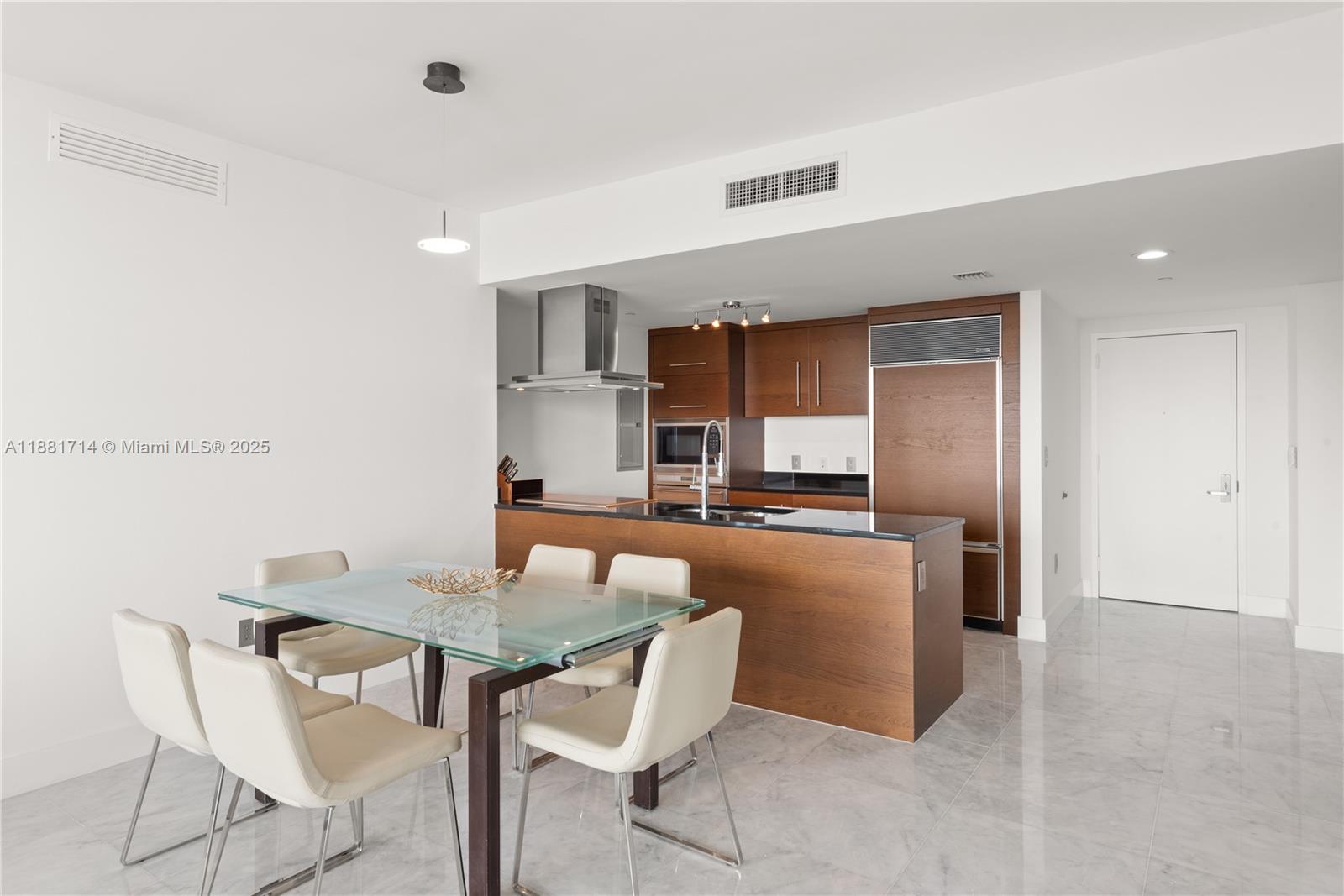 A dining area with a glass table sits adjacent to an open kitchen with wood cabinetry — 495 Brickell Ave # 5003, Miami FL 33131, MIAMI, FL