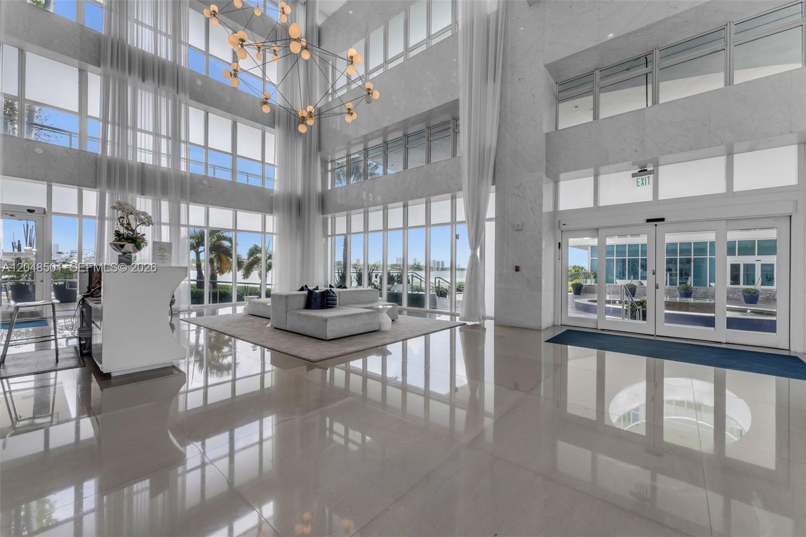 A modern, high-ceilinged lobby features marble floors, floor-to-ceiling windows, and a large contemporary chandelier — 520 West Ave # 604, Miami Beach FL 33139, MIAMI BEACH, FL