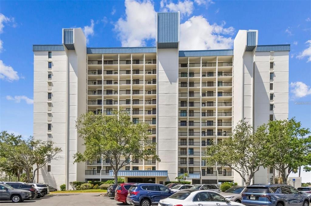 A multi-story residential building with balconies and a parking lot in the foreground — 9425 BLIND PASS ROAD UNIT 1006, ST PETE BEACH, FL