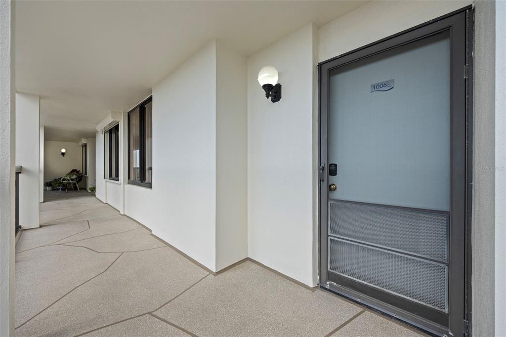 A view of an outdoor apartment hallway with a numbered door and a light fixture — 9425 BLIND PASS ROAD UNIT 1006, ST PETE BEACH, FL