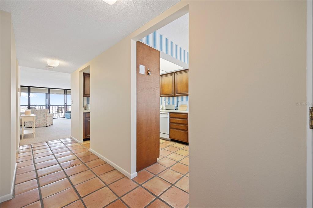 A tiled hallway leads to a kitchen with wood cabinets and a carpeted living area — 9425 BLIND PASS ROAD UNIT 1006, ST PETE BEACH, FL
