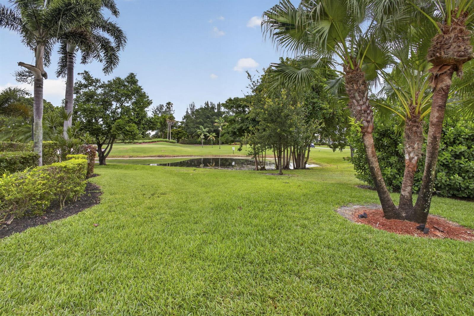A grassy lawn leads to a small pond surrounded by trees and palm trees — 6064 Beaconwood Road, Lake Worth FL 33467, LAKE WORTH, FL