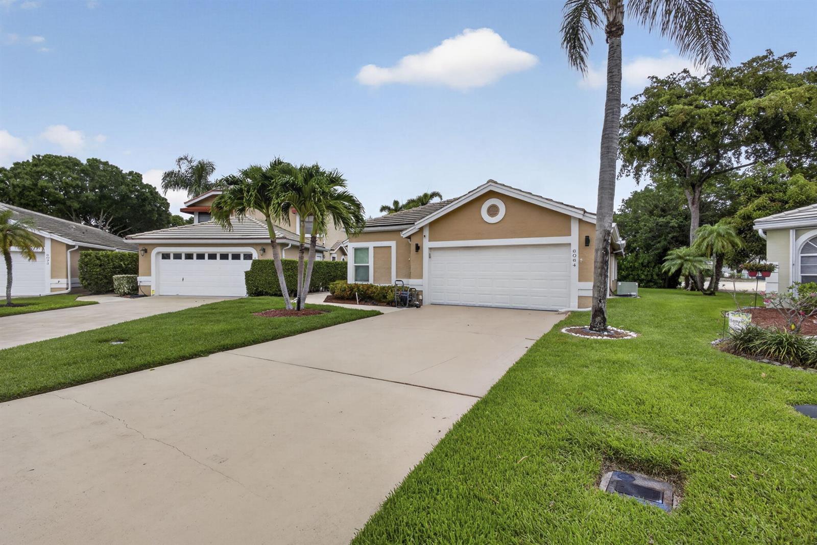 A tan single-story house with a white garage door and a palm tree in front — 6064 Beaconwood Road, Lake Worth FL 33467, LAKE WORTH, FL