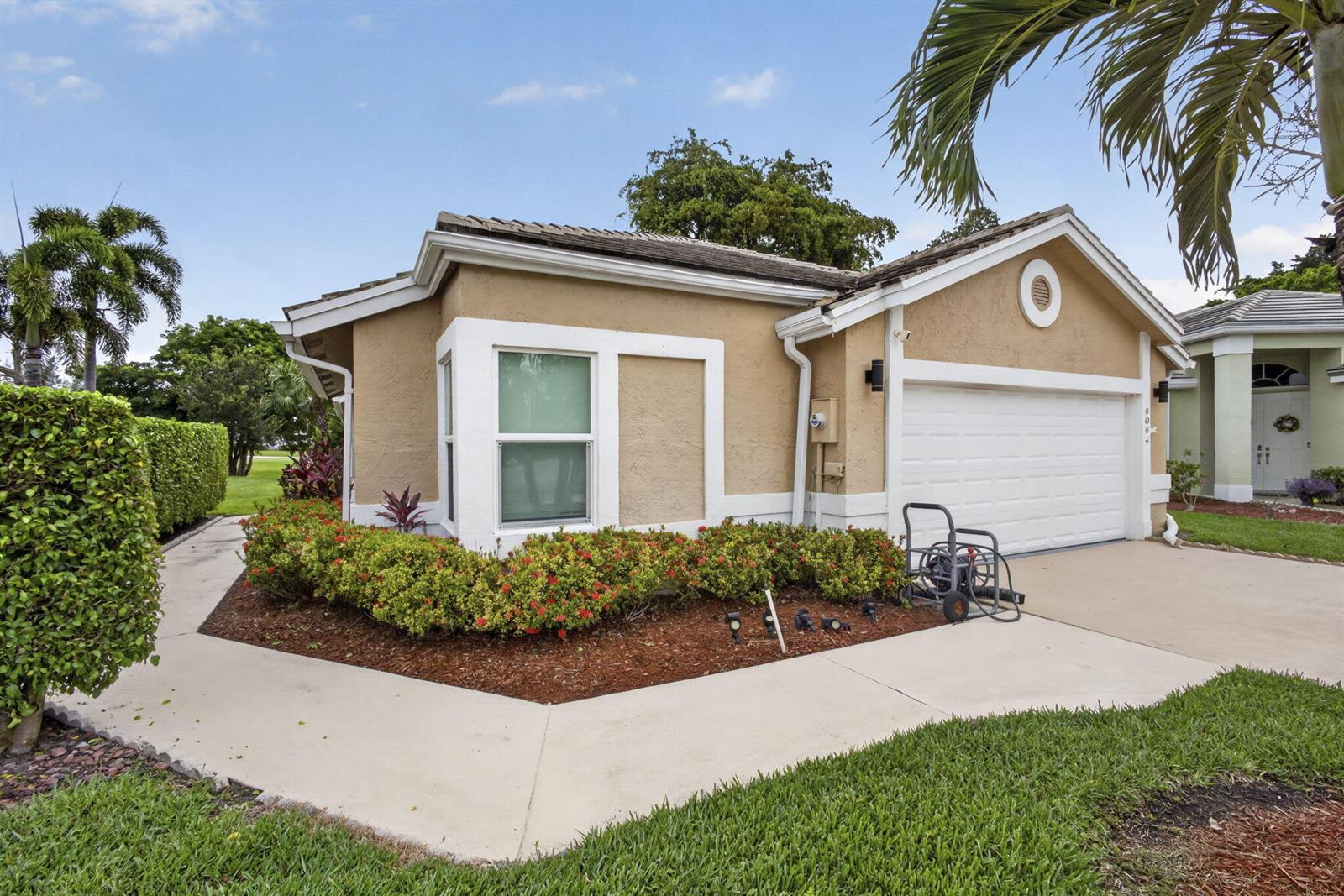 A tan single-story house with a white garage door and a landscaped front garden — 6064 Beaconwood Road, Lake Worth FL 33467, LAKE WORTH, FL