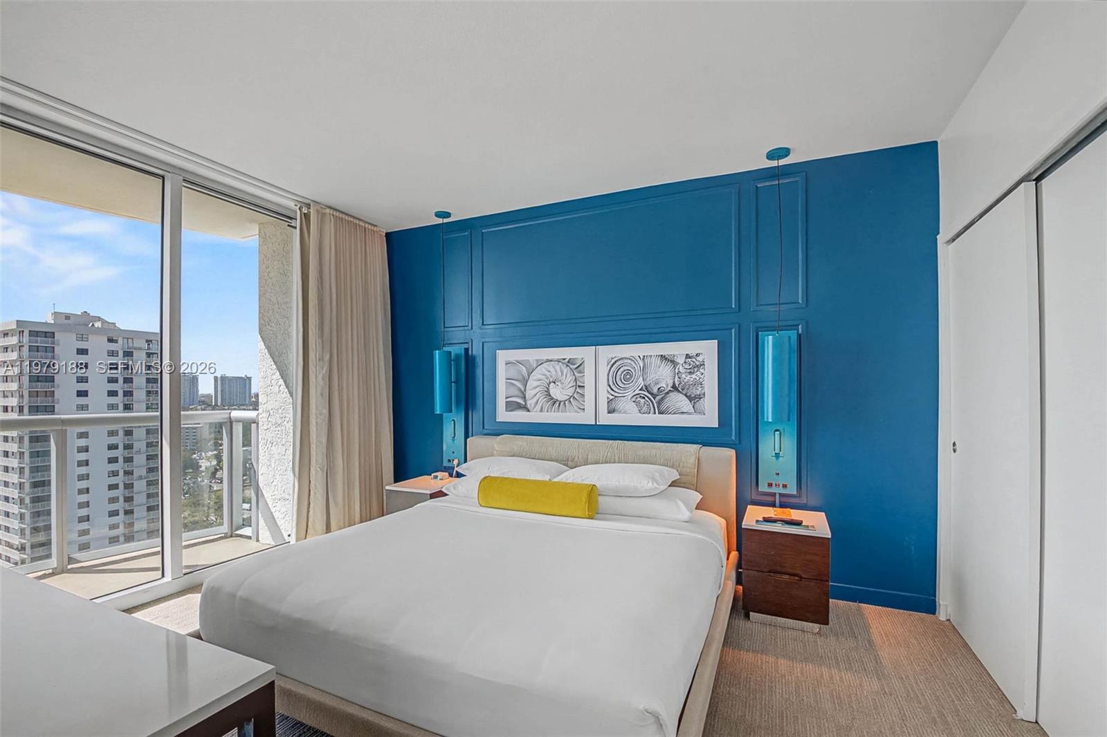 A bedroom features a blue accent wall with molding, a bed, and a balcony view — SUNNY ISLES BEACH, FL