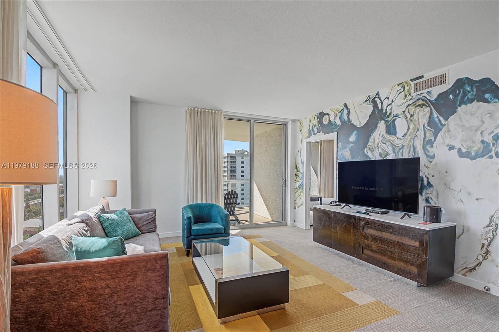 A living room features a patterned accent wall, a glass coffee table, and a balcony — SUNNY ISLES BEACH, FL