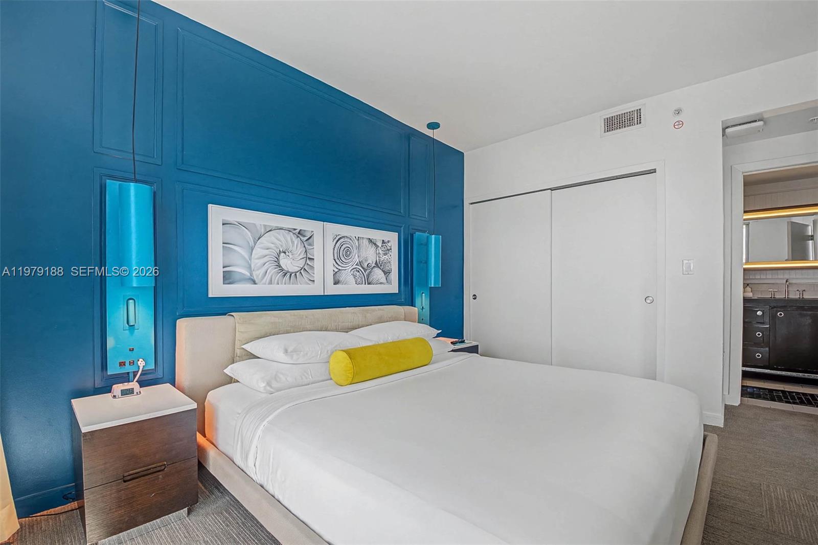 A bedroom features a blue accent wall, a bed with a yellow bolster, and carpet — SUNNY ISLES BEACH, FL