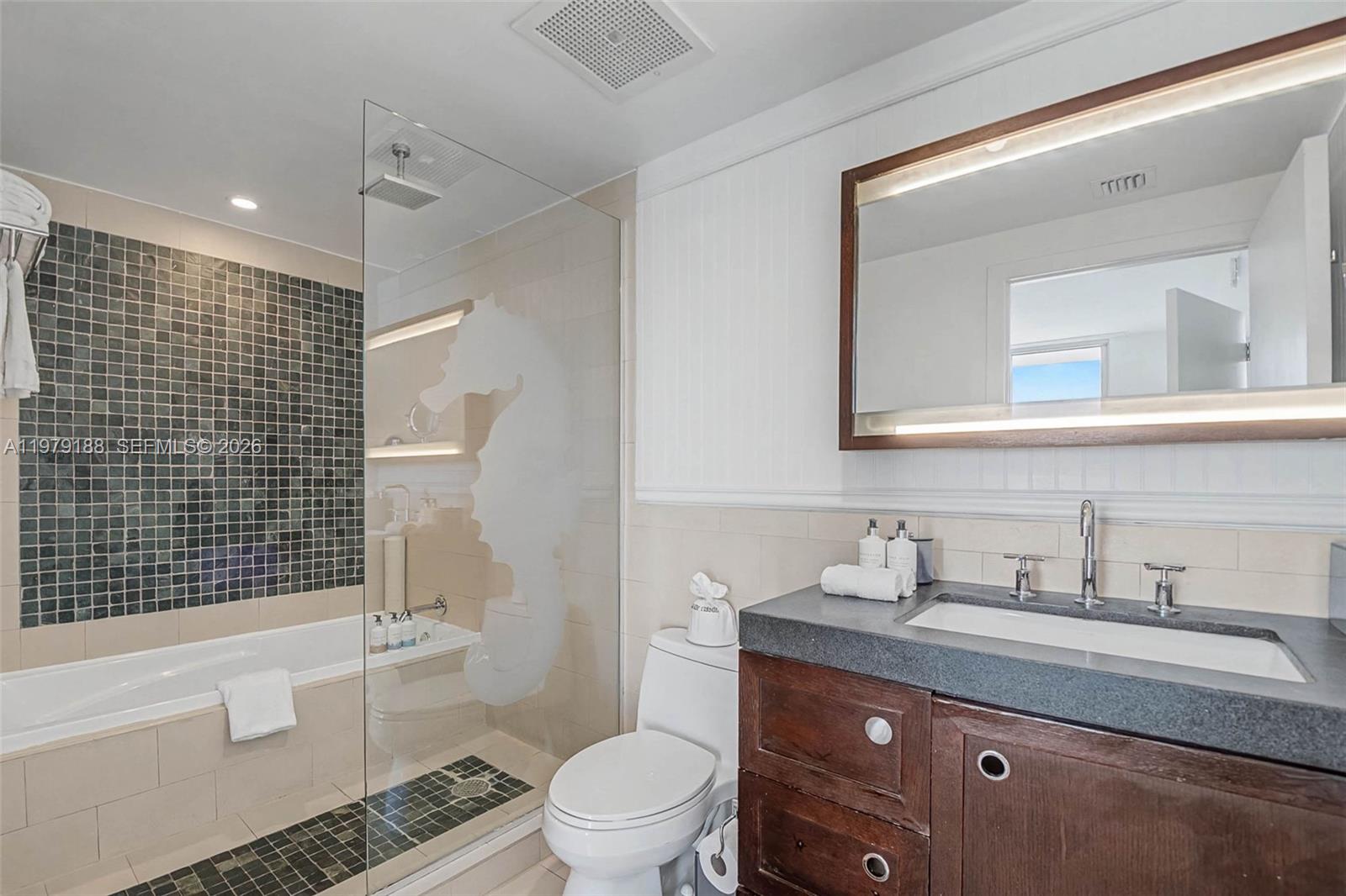 A bathroom features a dark wood vanity, a glass-enclosed shower, and a tiled bathtub area — SUNNY ISLES BEACH, FL