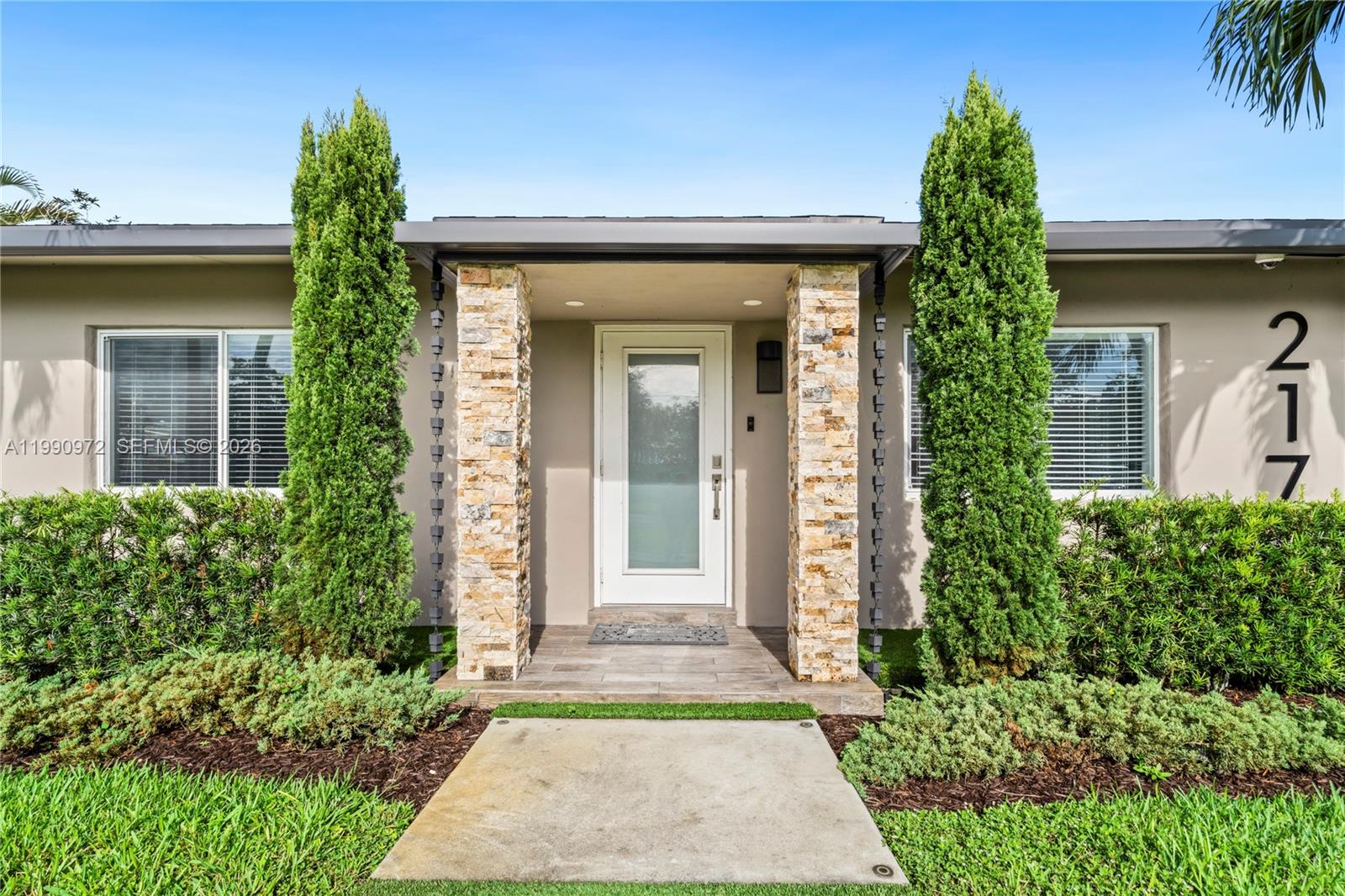 The exterior of a house features a stone-accented entryway, a white door, and two tall shrubs — 217 E Acre Dr, Plantation FL 33317, PLANTATION, FL