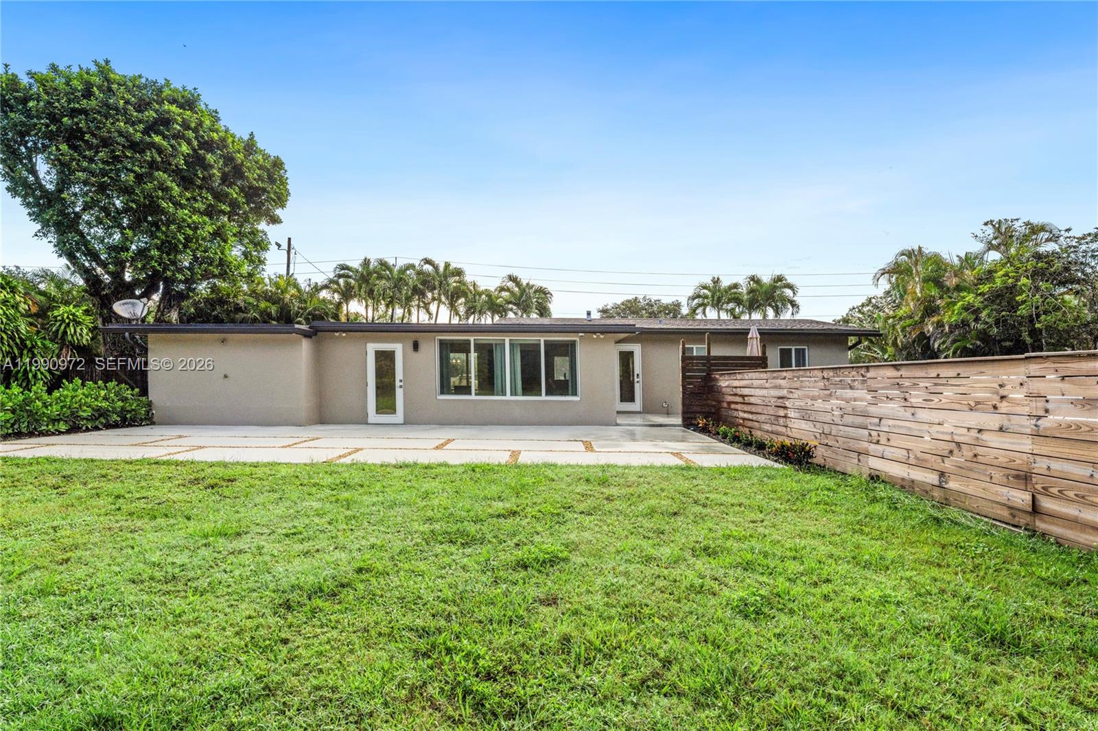 The exterior of a single-story house features a concrete patio and a wooden privacy fence — 217 E Acre Dr, Plantation FL 33317, PLANTATION, FL