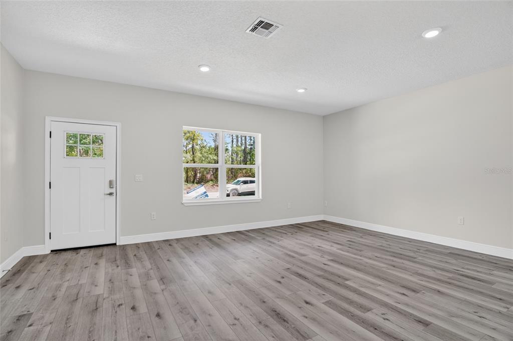An empty room features light gray walls, wood-look flooring, recessed lighting, and a white door — 7938 N MALTESE DRIVE, CITRUS SPRINGS, FL