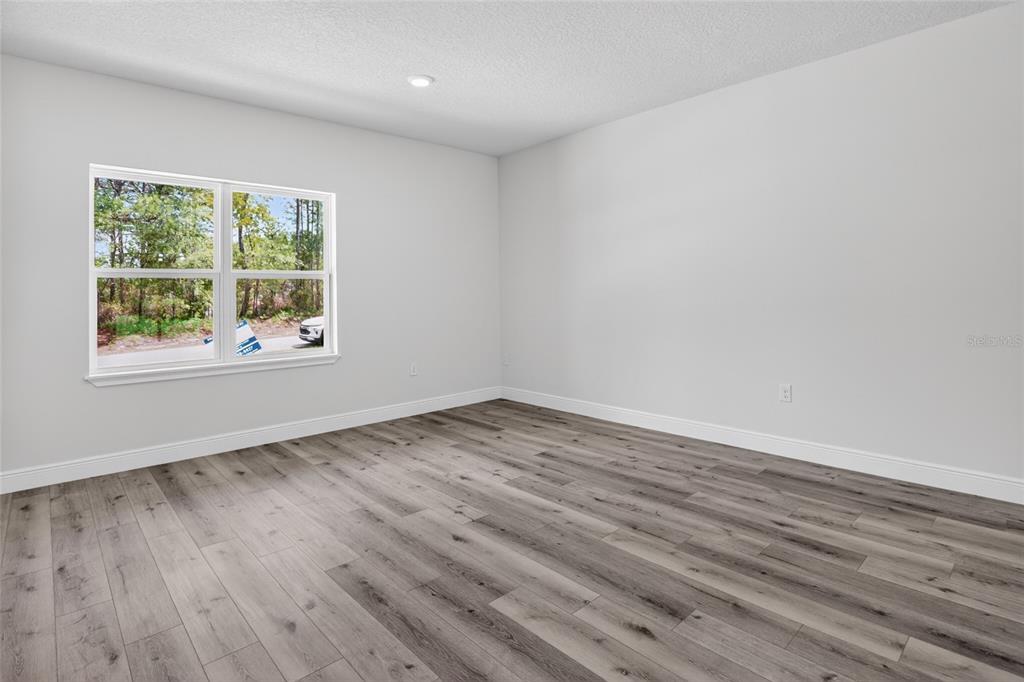 An empty room features light gray walls, wood-look flooring, and a window overlooking trees — 7938 N MALTESE DRIVE, CITRUS SPRINGS, FL