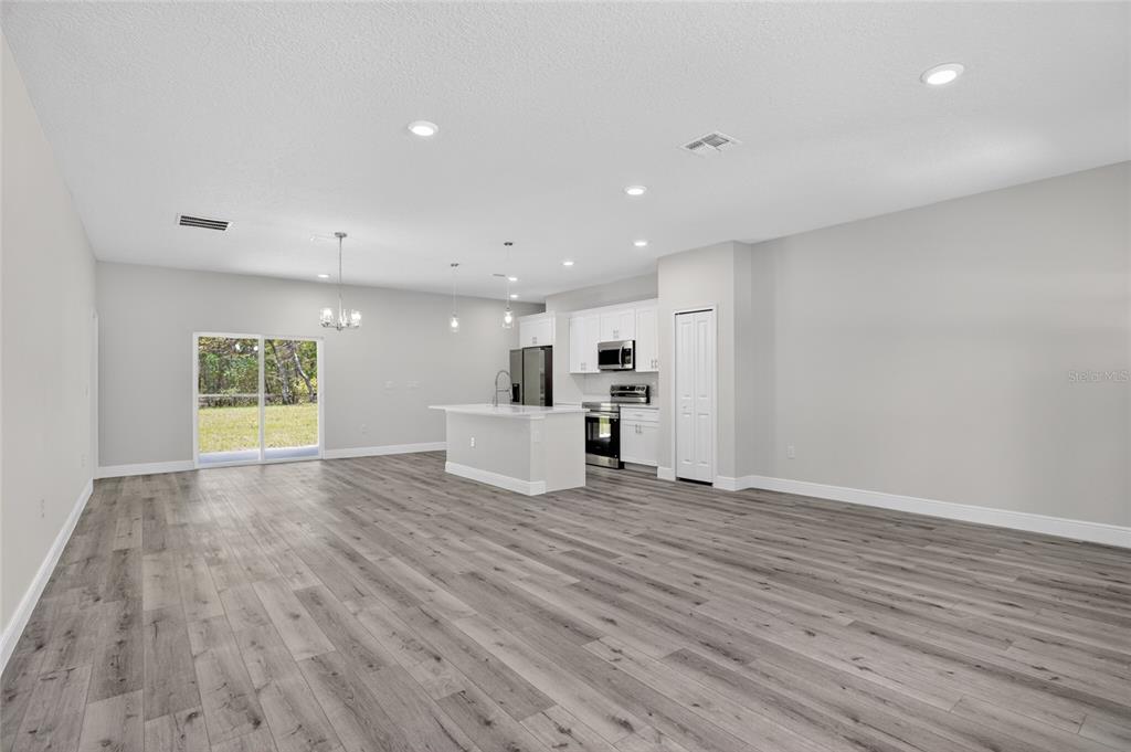 An open-concept kitchen and living area features gray wood-look flooring, white cabinetry, and sliding doors — 7938 N MALTESE DRIVE, CITRUS SPRINGS, FL