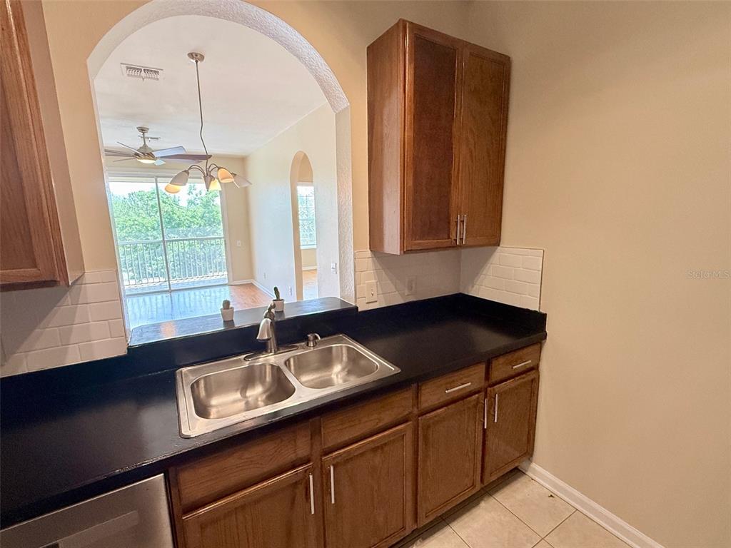 A kitchen features dark countertops, wood cabinets, a double sink, and a pass-through window — 3190 DANTE DRIVE UNIT 301, ORLANDO, FL