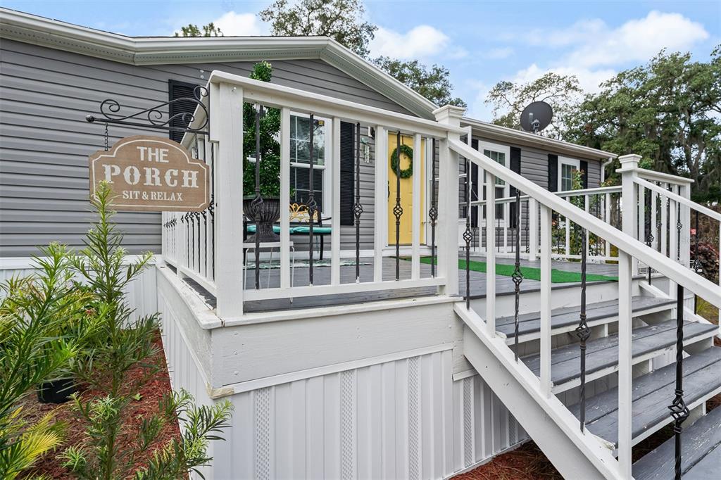 A gray house features a wooden porch with white railings, stairs, and a decorative sign — 8170 DOGYARD ROAD, LAKE WALES, FL