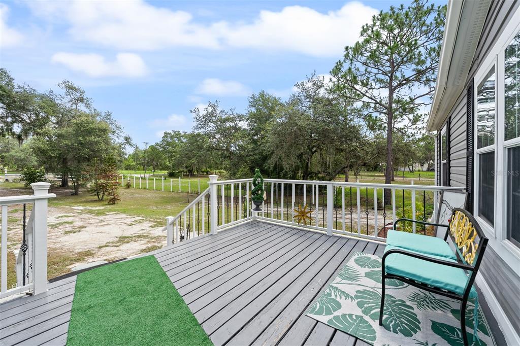 A wooden deck with a green mat and a bench overlooks a grassy backyard area — 8170 DOGYARD ROAD, LAKE WALES, FL