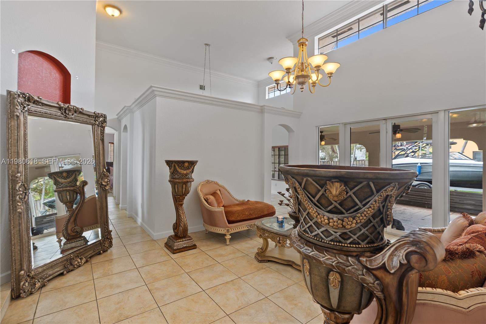 A high-ceilinged living room features tile flooring, ornate furniture, a large mirror, and glass doors — 12981 SW 197th St, Miami FL 33177, MIAMI, FL