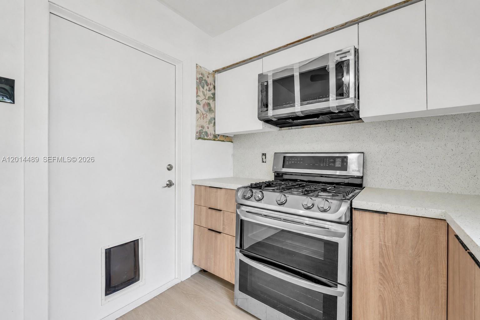 A kitchen features light wood cabinets, white countertops, a stainless steel stove, and a door — 1419 Harding St, Hollywood FL 33020, HOLLYWOOD, FL
