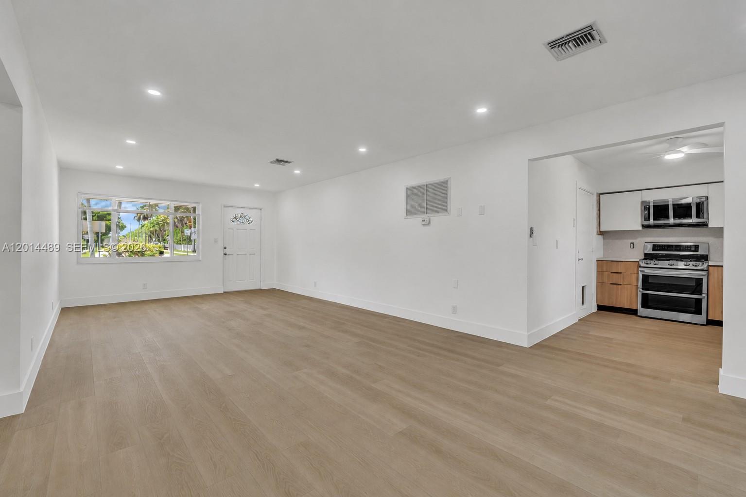 A bright, open-concept living area features light wood-look flooring and an adjacent kitchen — 1419 Harding St, Hollywood FL 33020, HOLLYWOOD, FL