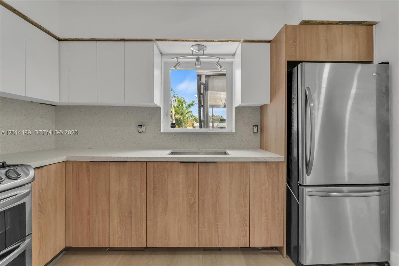 A kitchen features light wood lower cabinets, white upper cabinets, and a stainless steel refrigerator — 1419 Harding St, Hollywood FL 33020, HOLLYWOOD, FL