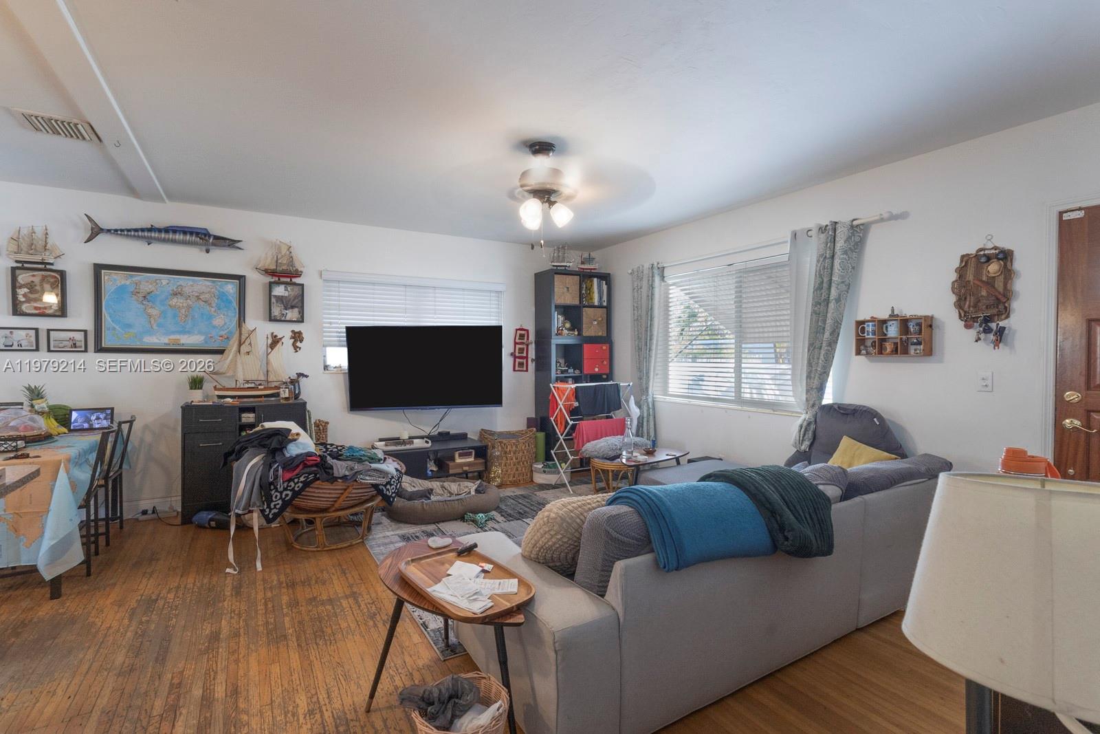 A living room with hardwood floors, a gray sofa, a wall-mounted television, and nautical decor — 2710 SW 28th Ct, Miami FL 33133, MIAMI, FL