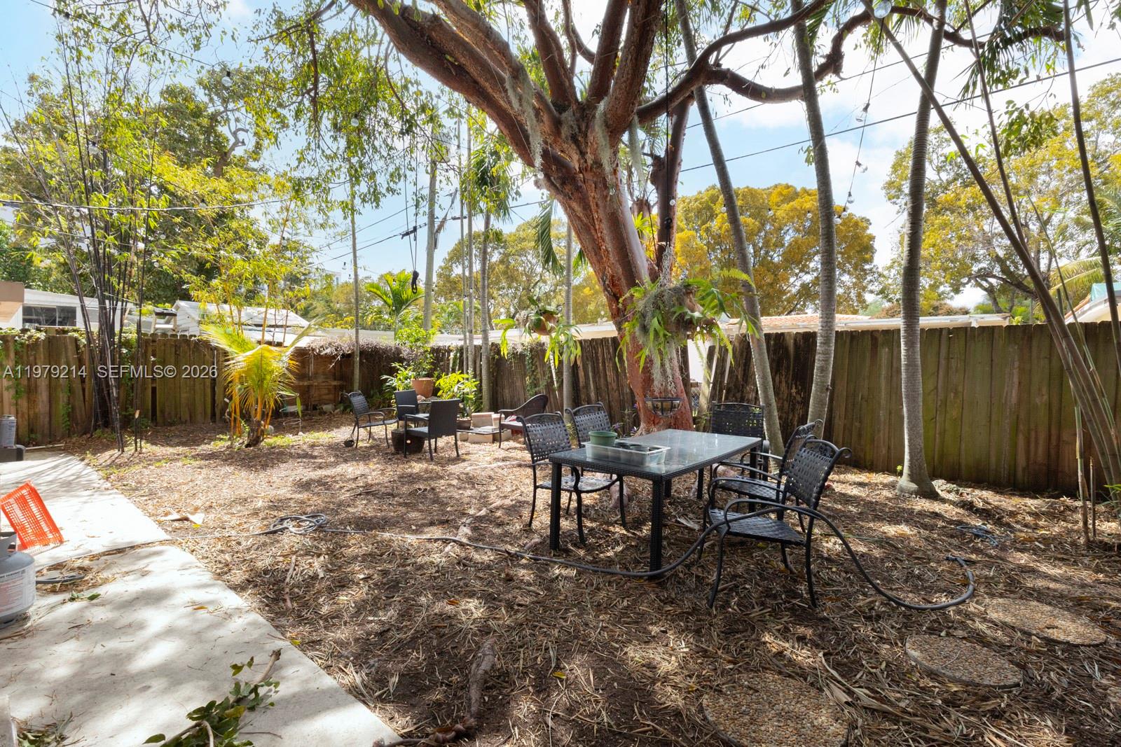 A backyard patio area features a dining set, mature trees, and a wooden fence — 2710 SW 28th Ct, Miami FL 33133, MIAMI, FL