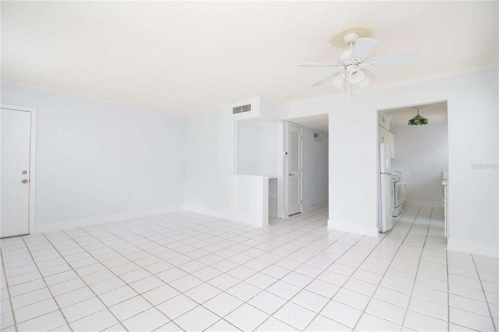 An empty room with white tile floors, a ceiling fan, and an adjacent kitchen area — 6960 A SUNSET DRIVE S UNIT 1C, SOUTH PASADENA, FL