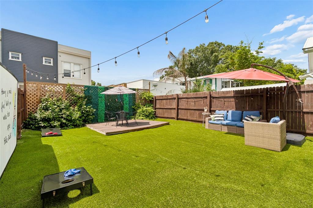 A fenced backyard features artificial turf, a wooden deck with a table, and patio furniture — 2307 E 11TH AVENUE, TAMPA, FL