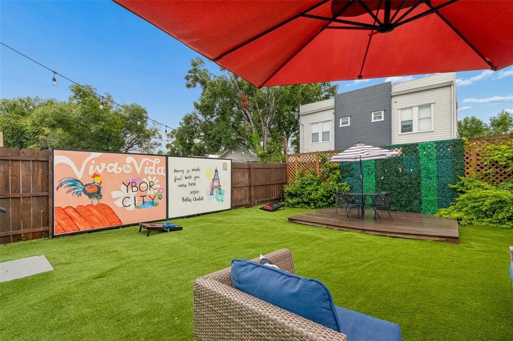 A fenced backyard features artificial turf, a wooden deck, outdoor seating, and a decorative mural — 2307 E 11TH AVENUE, TAMPA, FL