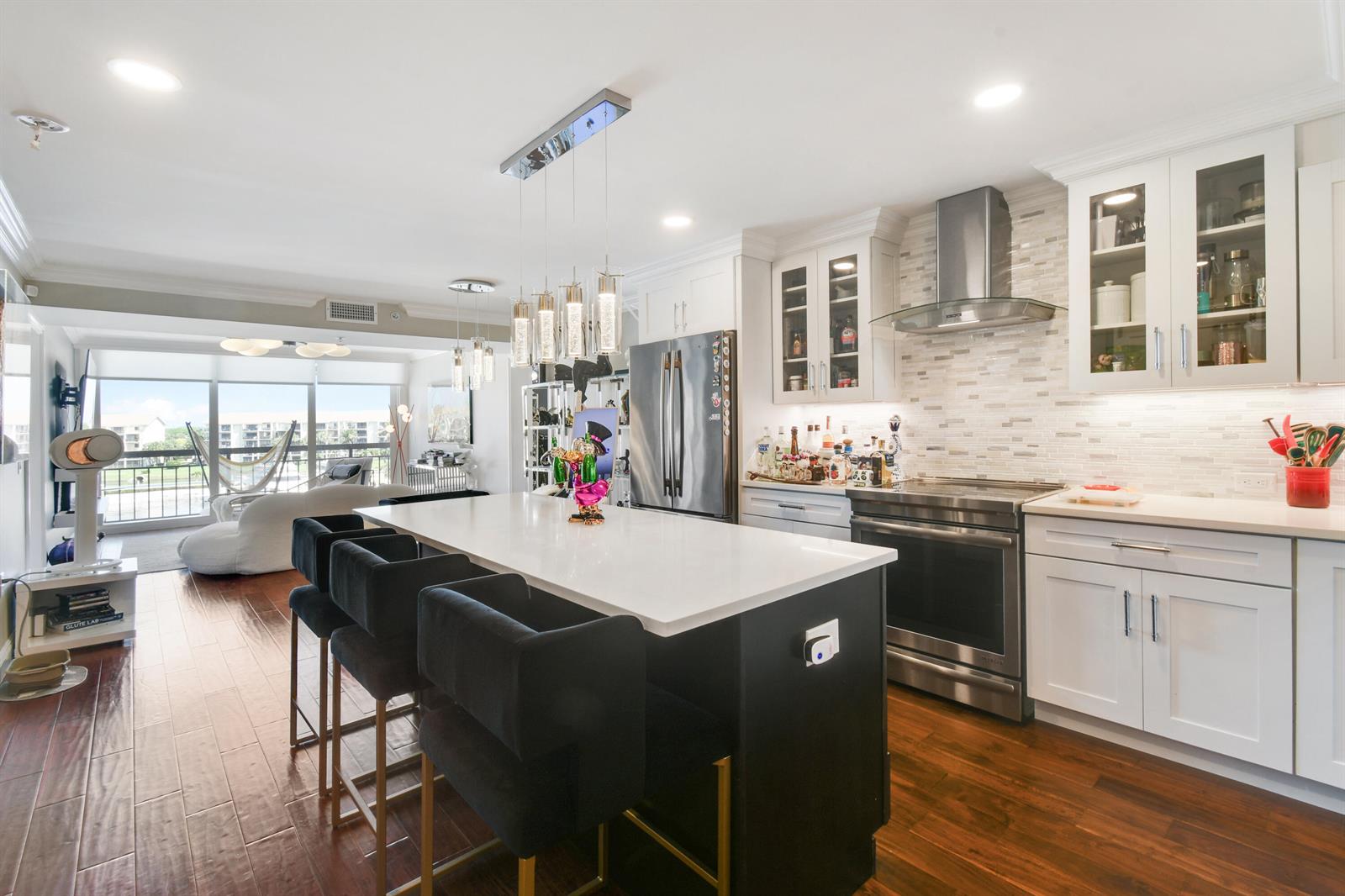 A modern kitchen features a dark island with bar stools, white cabinetry, and hardwood floors — 2401 Marina Isle Way # 503, Jupiter FL 33477, JUPITER, FL