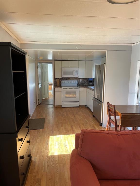 A kitchen with white cabinets and appliances opens to a living area with wood flooring — 6275 - A US HIGHWAY 441 SE, OKEECHOBEE, FL
