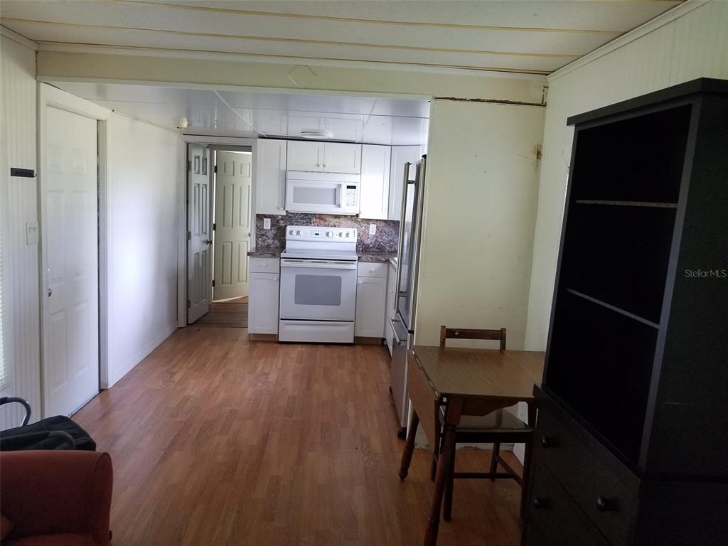 A kitchen features white cabinetry, a white stove, a stainless steel refrigerator, and wood flooring — 6275 - A US HIGHWAY 441 SE, OKEECHOBEE, FL