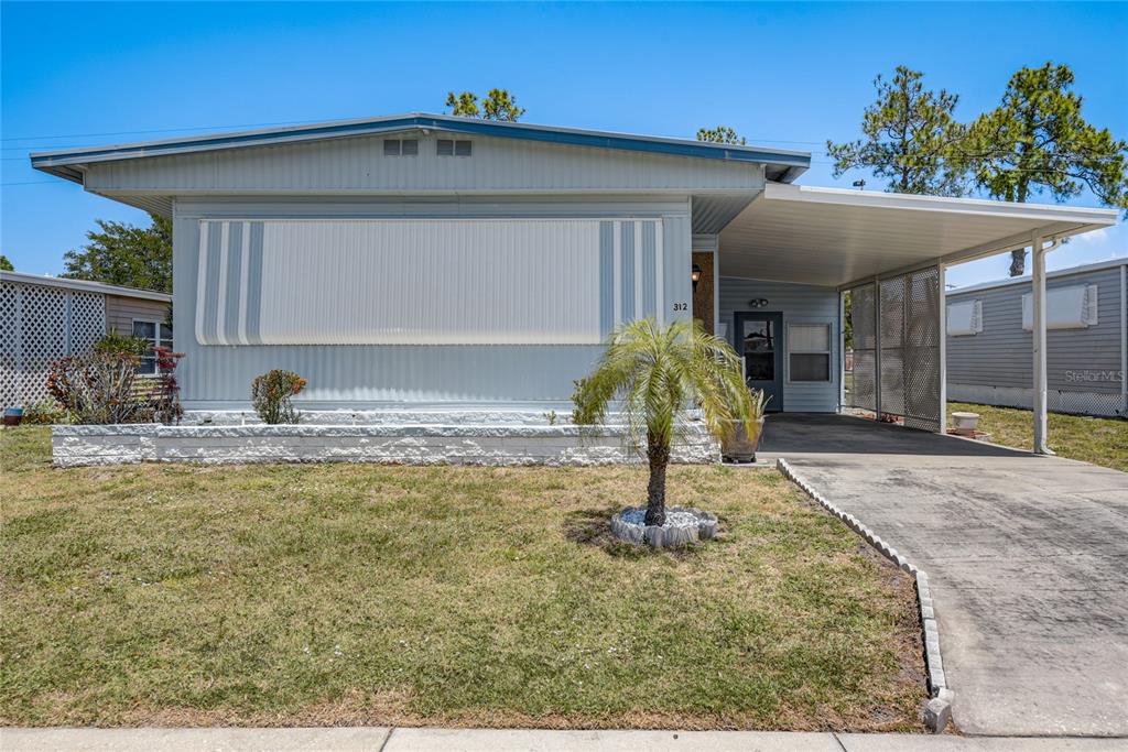A light blue manufactured home features a front awning, a carport, and a small palm tree — 5619 BAYSHORE ROAD UNIT 312, PALMETTO, FL