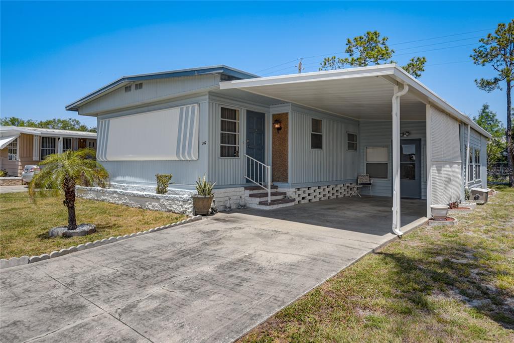 A light blue mobile home features a concrete driveway, a carport, and a small palm tree — 5619 BAYSHORE ROAD UNIT 312, PALMETTO, FL