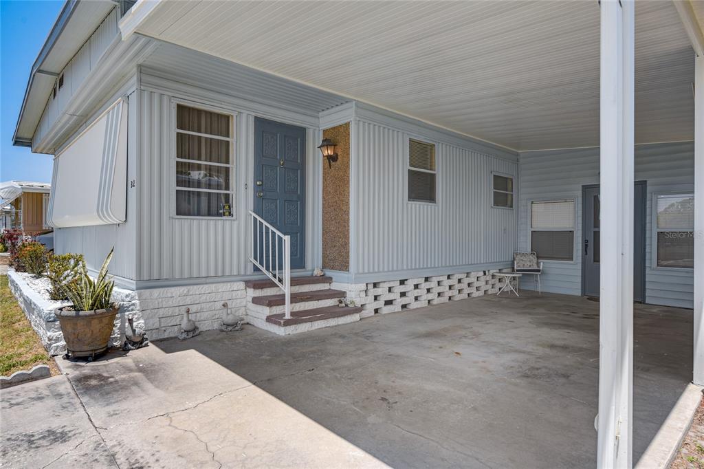 A light blue mobile home features a concrete carport, a front door, and brick skirting — 5619 BAYSHORE ROAD UNIT 312, PALMETTO, FL