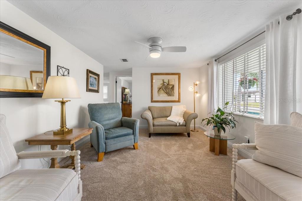 A living room features beige carpet, a ceiling fan, and several pieces of upholstered furniture — 3731 ELMWOOD DRIVE, HOLIDAY, FL