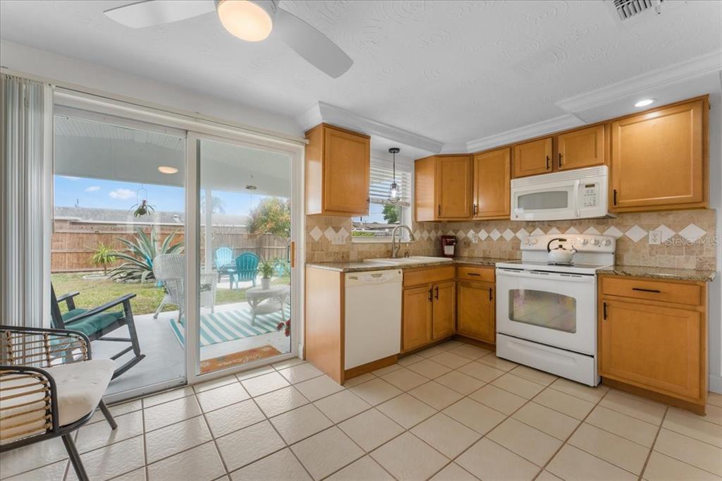 A kitchen with light wood cabinets, granite countertops, tile flooring, and a sliding glass door — 3731 ELMWOOD DRIVE, HOLIDAY, FL